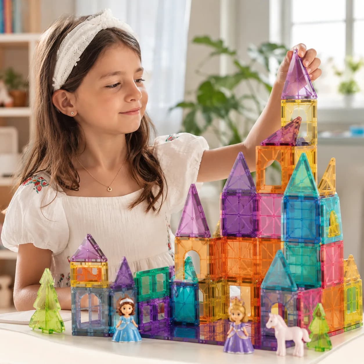 A girl building a castle from translucent magnetic tiles